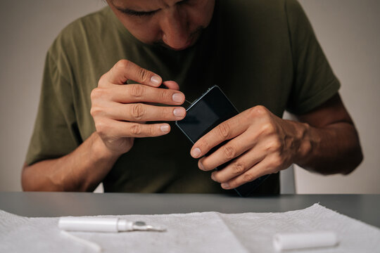 Close-up cropped shot of technician cleaning smartphone using specialized tools sitting at table, ensuring optimal quality and device performance. Concept of mobile phone maintenance and service.