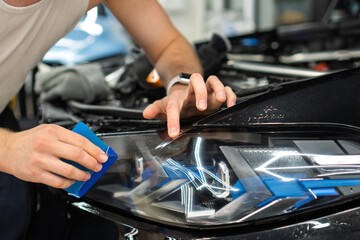 A car wrapping specialist applies a polyurethane film to the car. Selective focus. PPF protective film against chips and scratches. Car wrapping, detailing, tuning and styling. Detailer smoothes PPF. 