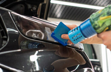 A car wrapping specialist applies a polyurethane film to the car. Selective focus. PPF protective film against chips and scratches. Car wrapping, detailing, tuning and styling. Detailer smoothes PPF. 