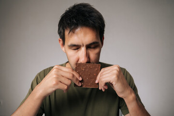 Studio portrait of enjoying young man savoring rich aroma of dark chocolate bar with closed eyes,...