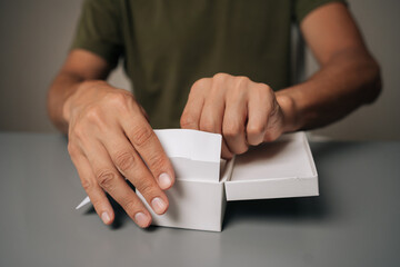 Close-up showing male hands unwrapping sleek electronic cigarette, revealing modern vaping device, precise handling and unboxing excitement. Concept of modern alternative to traditional smoking.