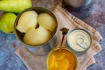 Canned pears and mandarin segments contrasted with two fresh pears, arranged on a rustic background. 