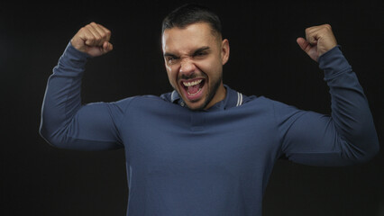 Naklejka premium Man flexes forearm and clenches fist to highlight muscle definition in black studio setting with dramatic lighting; triumph victory success winning.