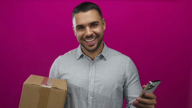 Man holding cardboard box and smartphone with both hands in studio against magenta backdrop examining package details; curiosity convenience efficiency innovation.