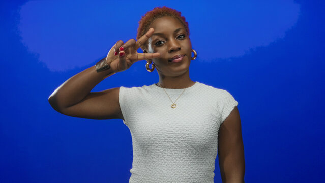 Woman with red manicure and gold hoop earrings holding peace sign with index and middle fingers in studio; serenity. - Powered by Adobe