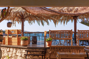 Outdoor beach bar with wooden furniture, potted plants and a straw roof overlooking the sea. Concept of vacation design, travel marketing and summer lifestyle.