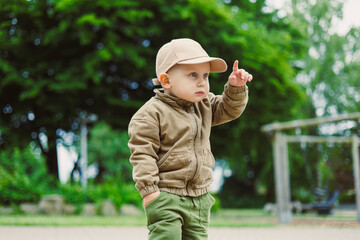 Little boy exploring the park in his cozy outfit while pointing towards something exciting under a...