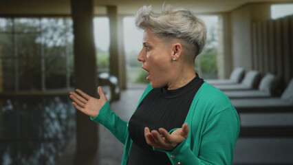 Woman with grey hair spreads palms and gasps at luxury modern indoor spa pool with lounge chairs; astonishment.