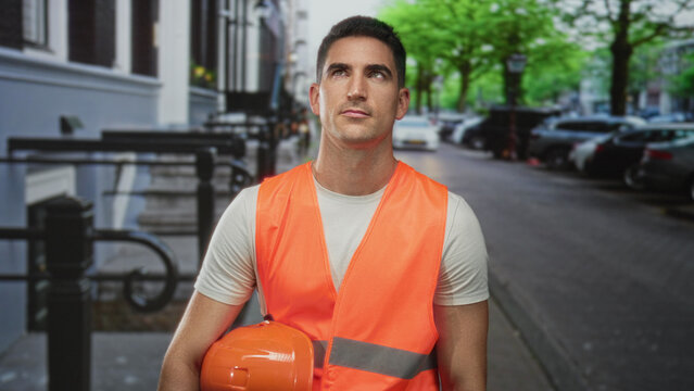 Man engineer holding hardhat and wearing high visibility vest on street; determination safety duty professionalism.