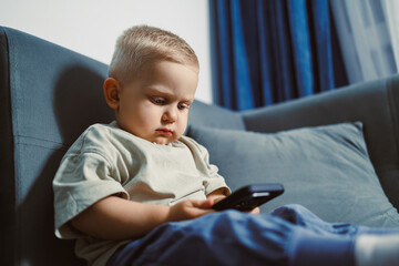 Young child focused on a smartphone while sitting comfortably on a cozy couch in a softly lit living room