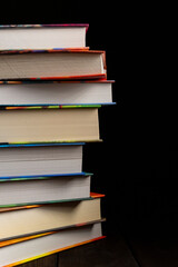 Vertical stack of hardcover books with colorful edges on black background