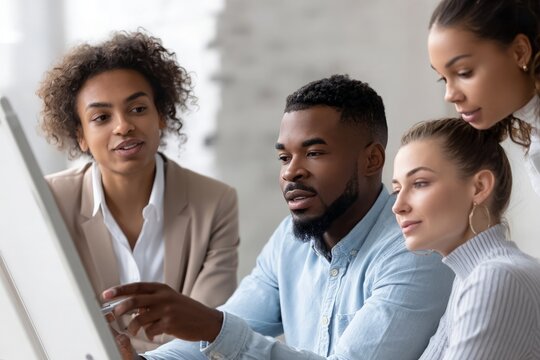 African American man pointing at screen, African American woman and diverse team discussing project in office.