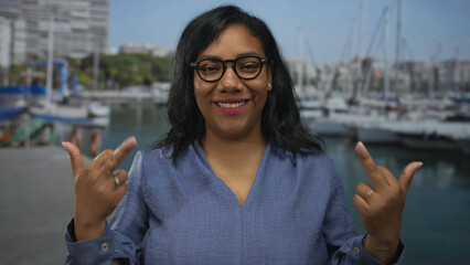 African american woman smiling wearing blue shirt shows middlefinger near boat and building;...
