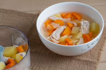 Homemade chicken soup ingredients in blender and bowl