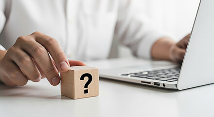 Person ponders a question mark block next to a laptop on a white desk seeking answers and solutions for business or personal challenges