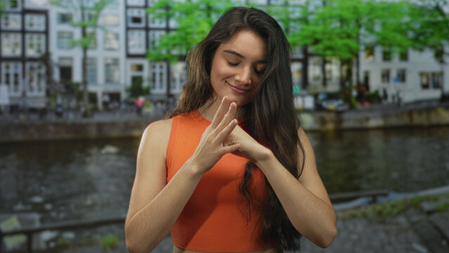 Young hispanic woman slams fist against palm on street by river canal lined with buildings; anger frustration.