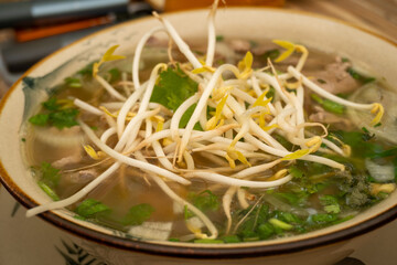 Close-up of a steaming bowl of Vietnamese pho noodle soup with fresh bean sprouts and herbs.