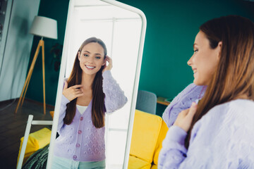 Joyful woman in lilac cardigan admires her reflection in a full length mirror at home living room creating a warm and stylish everyday moment © deagreez