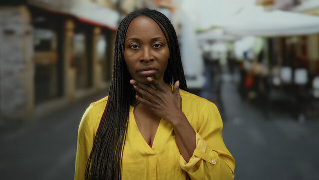 Woman contemplating on a terrace with street cafe ambiance, wearing yellow, showcasing serene outdoor setting and black hair.