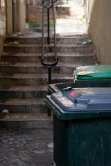 Grungy Alleyway with Stairs and Overflowing Trash Bins.