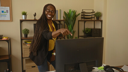 Woman dancing joyfully in office with plants glasses wearing vibrant clothing expressing lively energy.