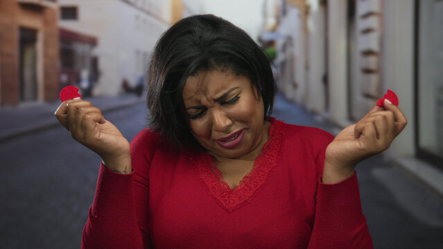 Woman wearing red shirt expressing heartbreak with paper heart on a city street.