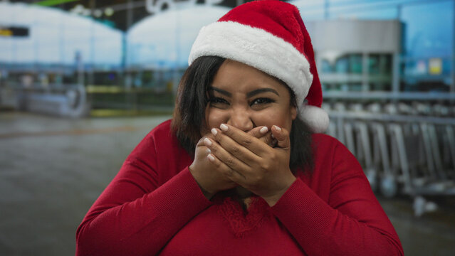 Woman wearing santa hat laughing in airport terminal with festive cheer, showcasing joyful holiday moment indoors with blurred background of airport setting. - Powered by Adobe