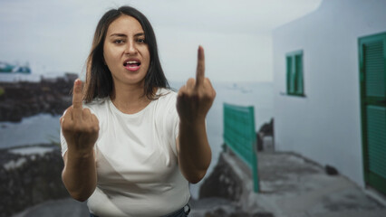 Woman showing middle finger with both hands on street by seaside promenade outdoors; defiance rebellion.