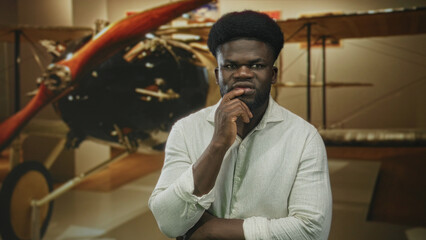 Man hand on chin in museum building beside vintage airplane propeller, looking pensive and studying...
