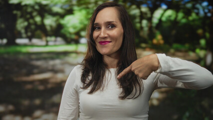 Fototapeta premium Woman giving thumbs up confidently in a lush green park setting, embodying positivity and success with a friendly smile outdoors.