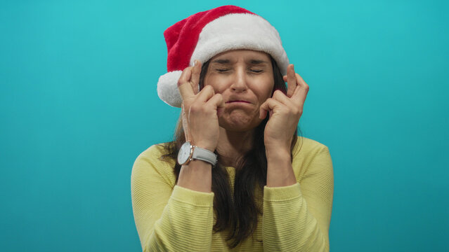 Woman in santa hat crossing fingers on green wall background hoping for christmas wish to come true with cheerful expression, isolated from other distractions.