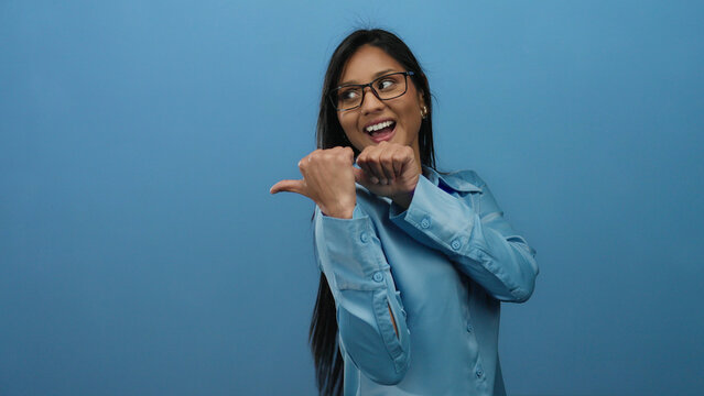 Woman playfully pointing in a stylish blue outfit with isolated blue background showing dynamic expression