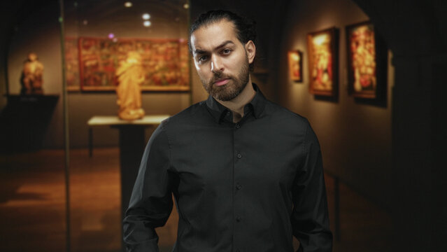 Man tilts head while standing in a gallery building, face forward and hands relaxed at sides; contemplation.
