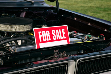 Old vehicle parked with its hood open and a red “For Sale” sign displayed on the front