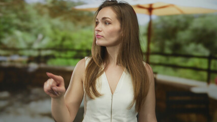 Obraz premium Young woman finger pointing to side on sunny building terrace overlooking green trees; determination.