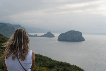 Frau mit langen Haaren blickt auf die neblige Atlantikküste im Baskenland, Nordspanien, mit...
