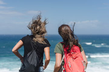 Zwei Frauen mit Rucksäcken stehen an der windigen Atlantikküste im Baskenland, Nordspanien,...