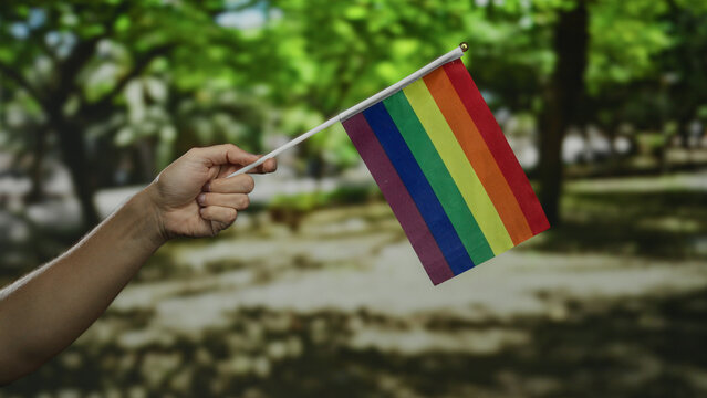Hand of caucasian man holding lgbtq flag in outdoor park setting symbolizes pride and diversity - Powered by Adobe