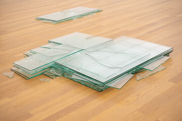 Zerbrochene Glasscheiben liegen auf einem Parkettboden, feine Risse und Bruchlinien, abstrakt