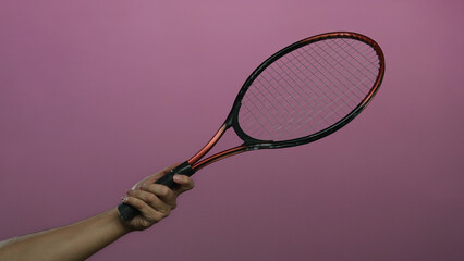 Man holding tennis racket against pink wall showing isolated hand and sports equipment in a...