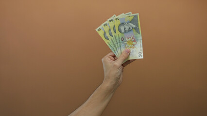 Hand of a caucasian man holding romanian lei banknotes against a brown wall background, emphasizing...