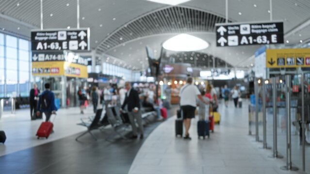 Blurred airport terminal interior with shallow bokeh, defocused signage and rolling luggage in soft focus; background backplate copyspace template.