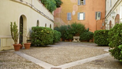 Roman courtyard plaza blurred bokeh background with potted shrubs, hedges and cobblestone paving;...