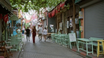 Narrow market alley in soft bokeh with defocused cafe tables, shutters, flags and overhead trees; backdrop copyspace backplate.