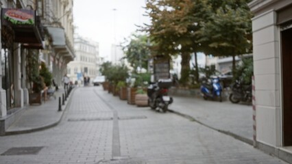 Blurred urban street scene with defocused storefronts, planters and scooters in shallow focus street; backdrop copyspace backplate template.