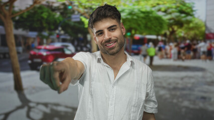 Fototapeta premium Hispanic man in white linen shirt smiles and points finger toward camera in sunlit street; confidence.
