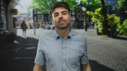 Man wearing a buttoned shirt tilting head with slight smile showing face on a sunlit city street; serenity.