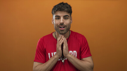 Hispanic young lifeguard man with whistle clasping hands and standing poised in studio; calm...