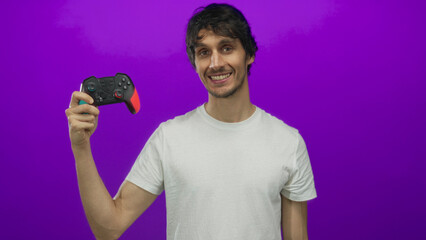Man holding game controller with colored grips in purple studio; digital entertainment excitement fun.