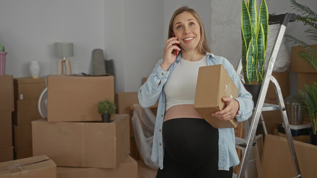 Pregnant woman talking on phone holding box in new home living room surrounded by moving boxes and plants. - Powered by Adobe